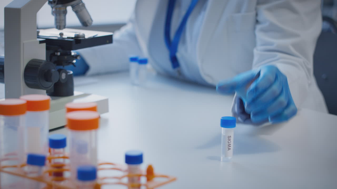 Close Up Of Lab Worker Conducting Research Using Microscope Holding Test Tube Labelled Sigma