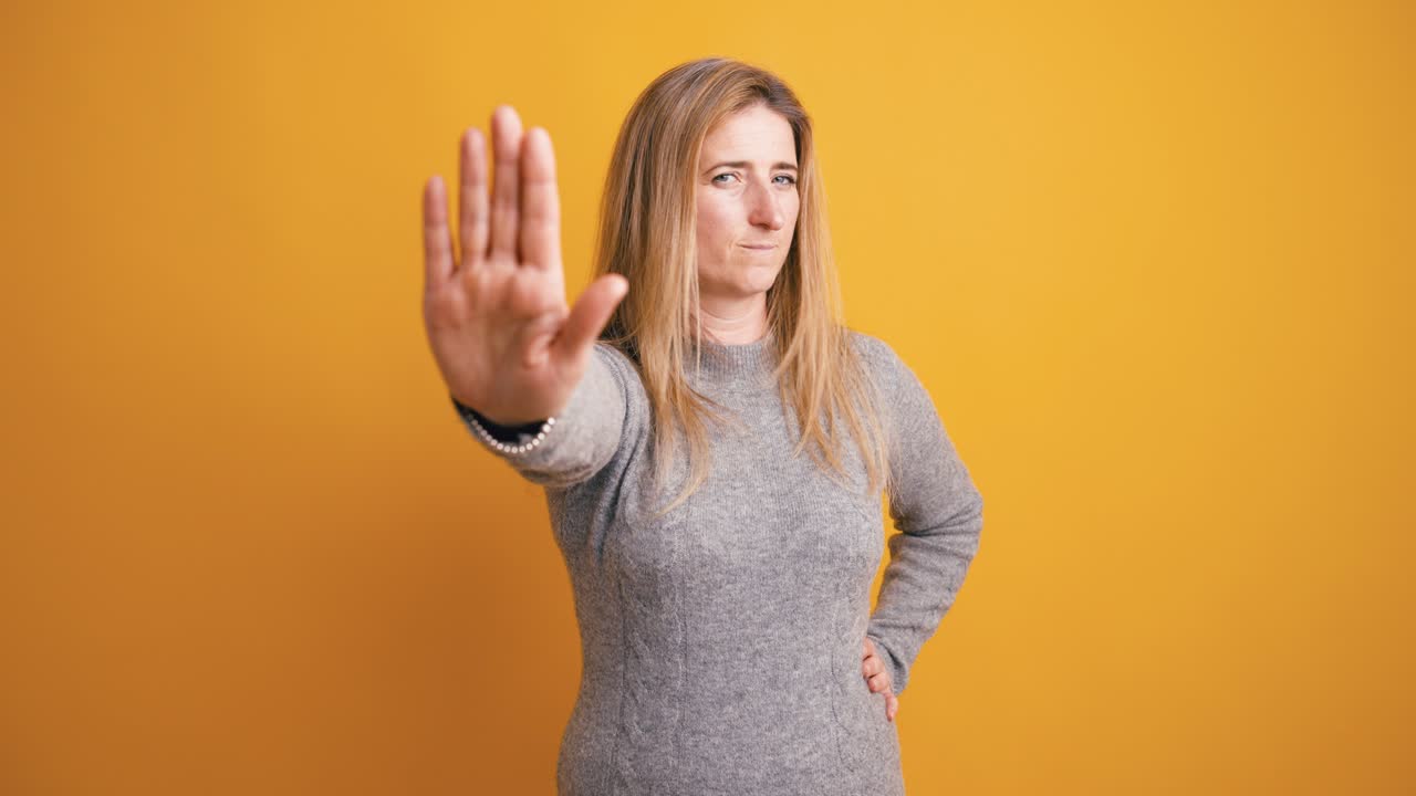 Serious Woman Making Stop Hand Gesture on Yellow Background