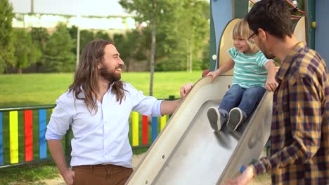 two men and a child playing on a slide at a park