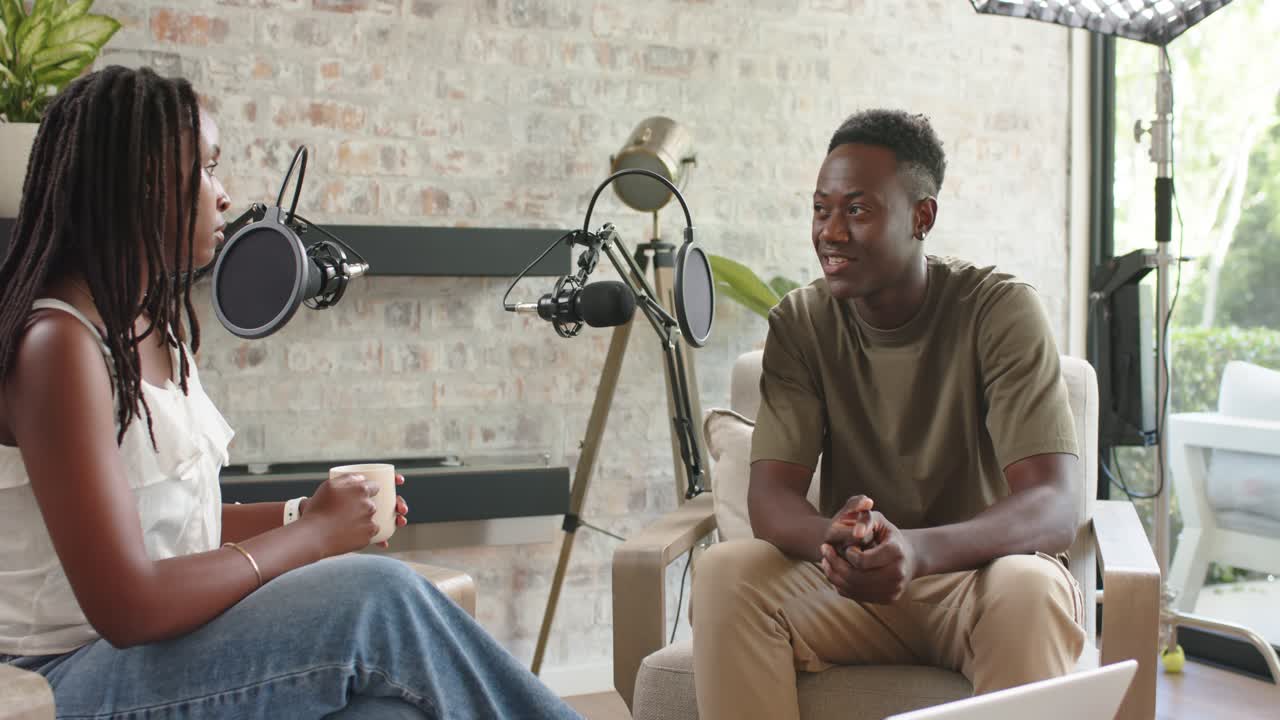 African American hosts sitting home studio microphones recording woman holding mug man gesturing