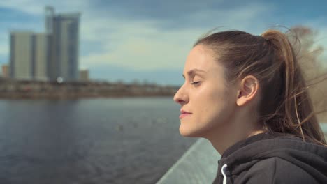 Young-Beautiful-Brunette-Woman-Enjoying-The-Peace-And-Nice-Breeze-By-The-Water,-Inhaling-Deep-Breath-Of-Fresh-Air-While-Soaking-In-The-Sun-And-Calmness-Of-The-River