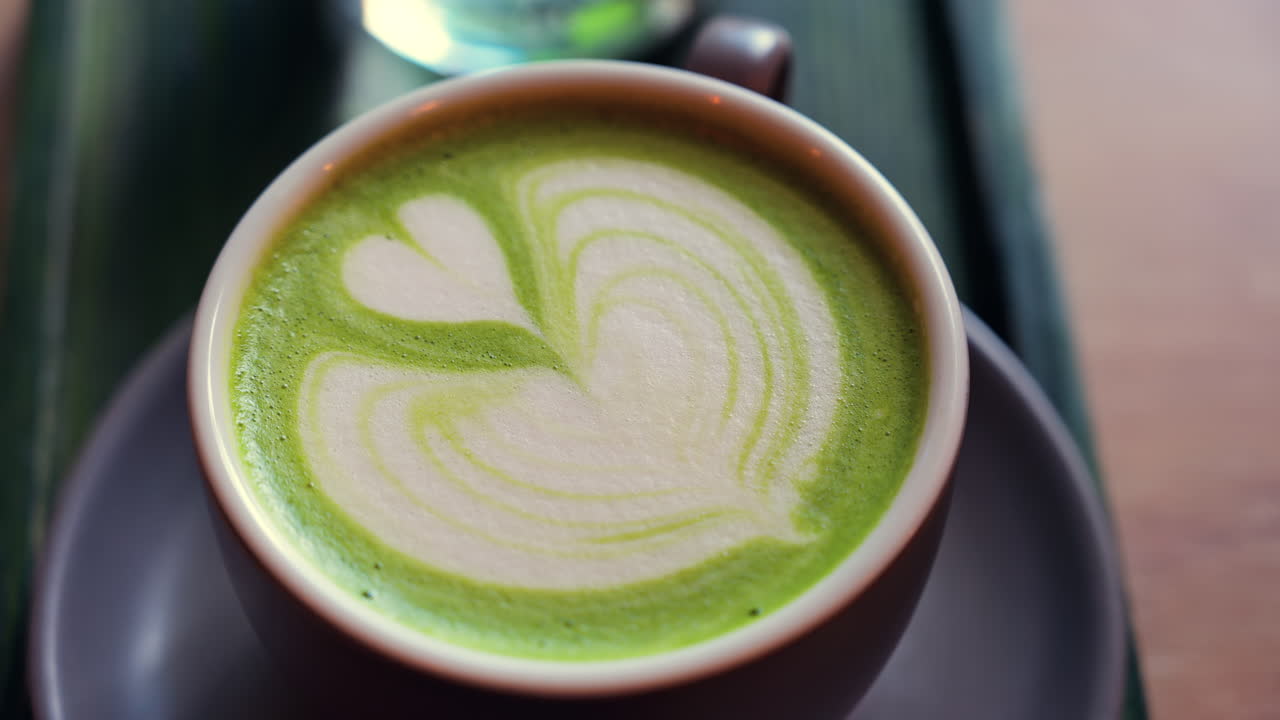 Close up of a matcha latte and a glass of water on a little green tray on a table at a cafe