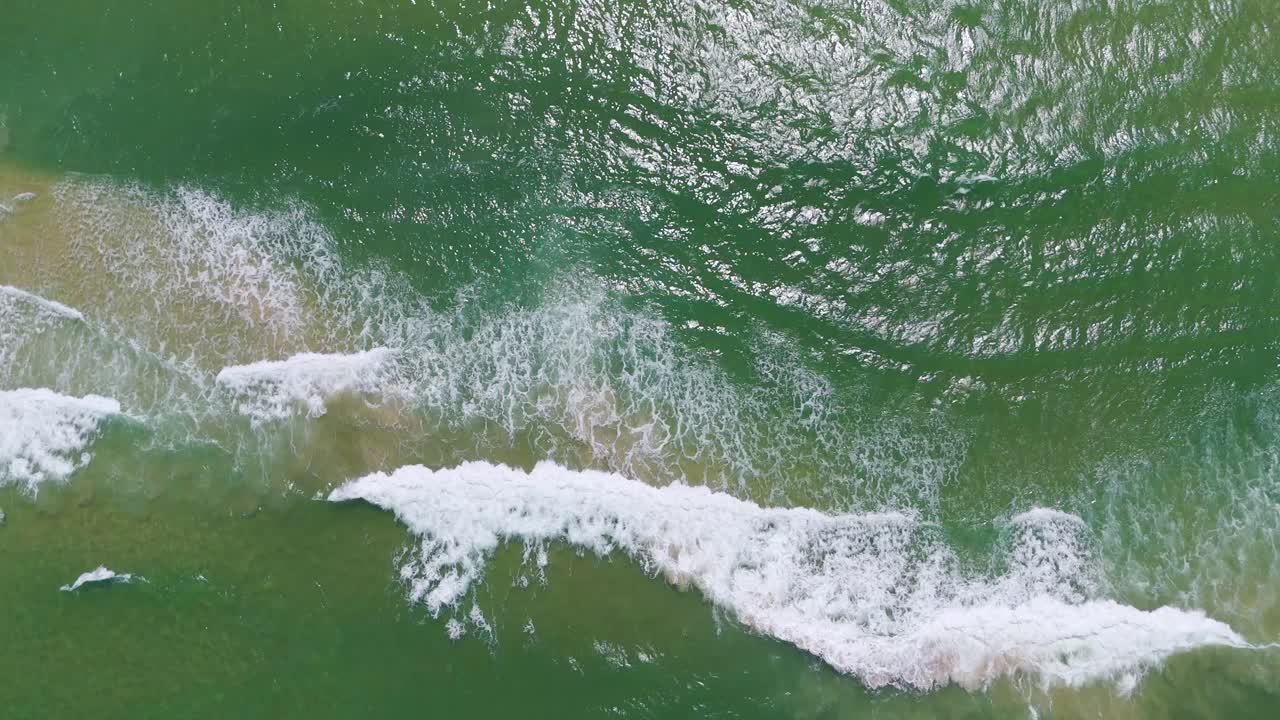 el dron captura las olas que se estrellan en la orilla arenosa.