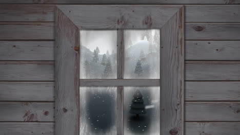 wooden window frame against snow falling over multiple trees on winter landscape