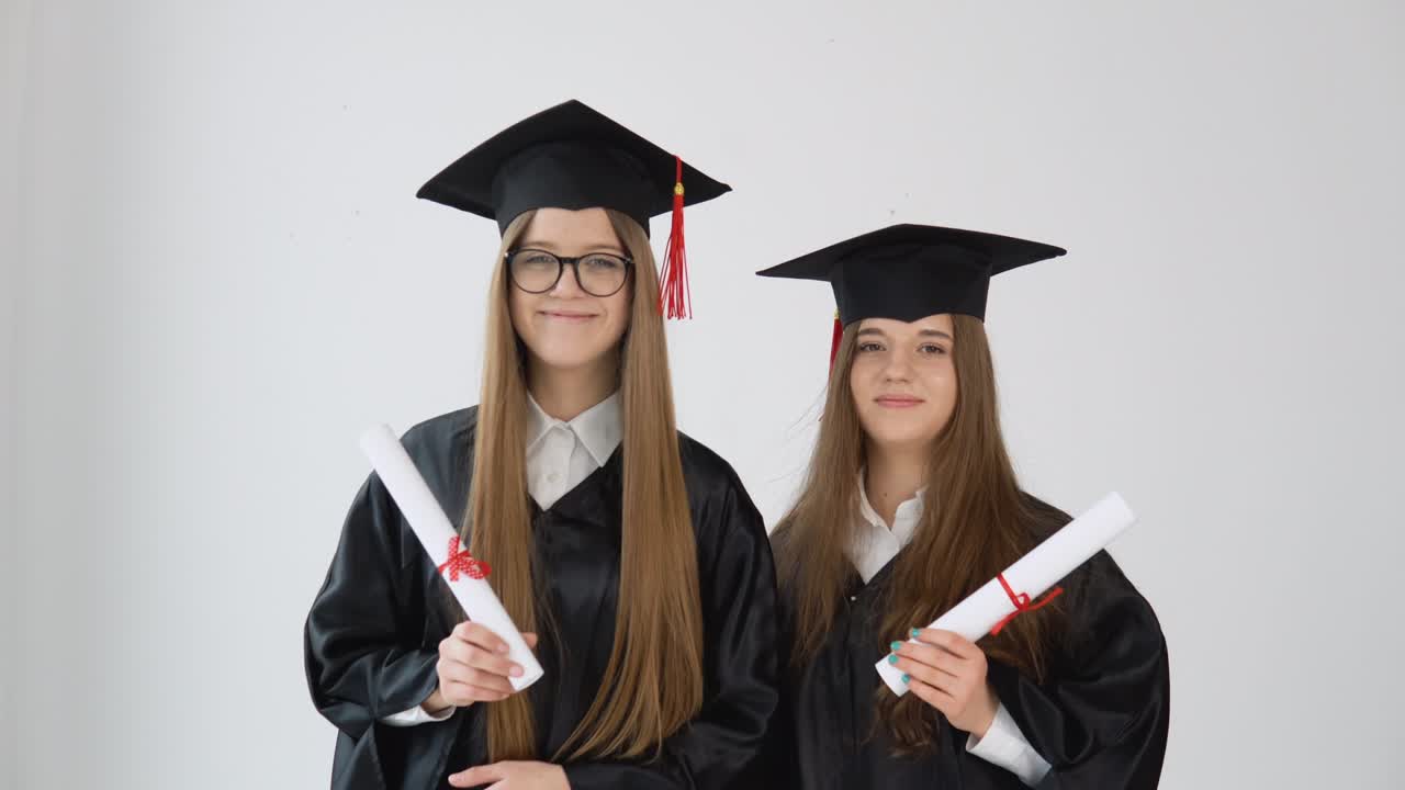 dos jóvenes graduadas felices de pie hombro a hombro con diplomas de graduación en sus manos. vista de cerca en fondo blanco