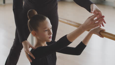 gymnastic blonde girl rehearsing a ballet move in front of ballet barre 3