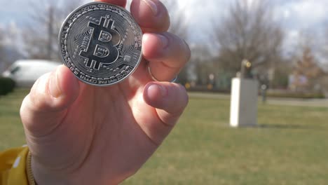 token de bitcoin con la estatua de satoshi nakamoto en el fondo