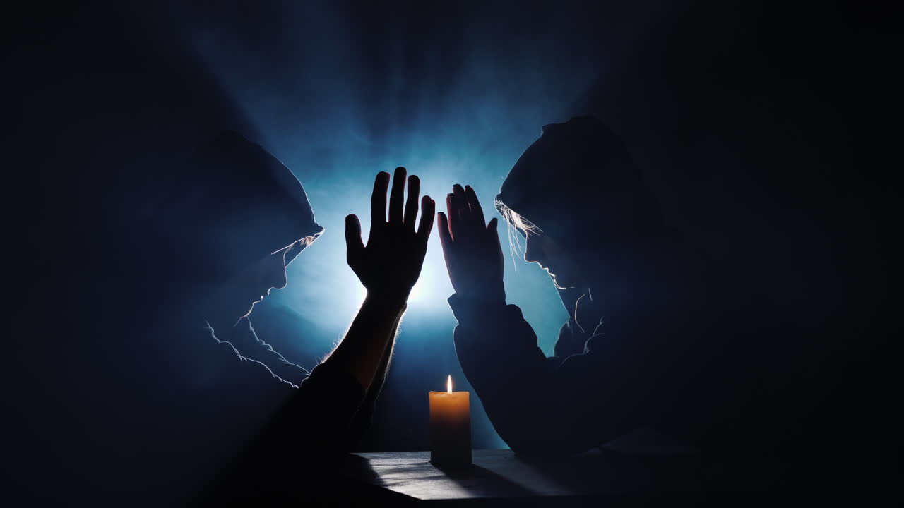 dos hombres encapuchados rezan en la oscuridad en los rayos de luz