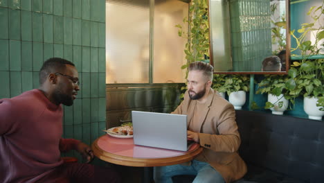 multiethnic businessmen meeting in cafe and discussing project on laptop