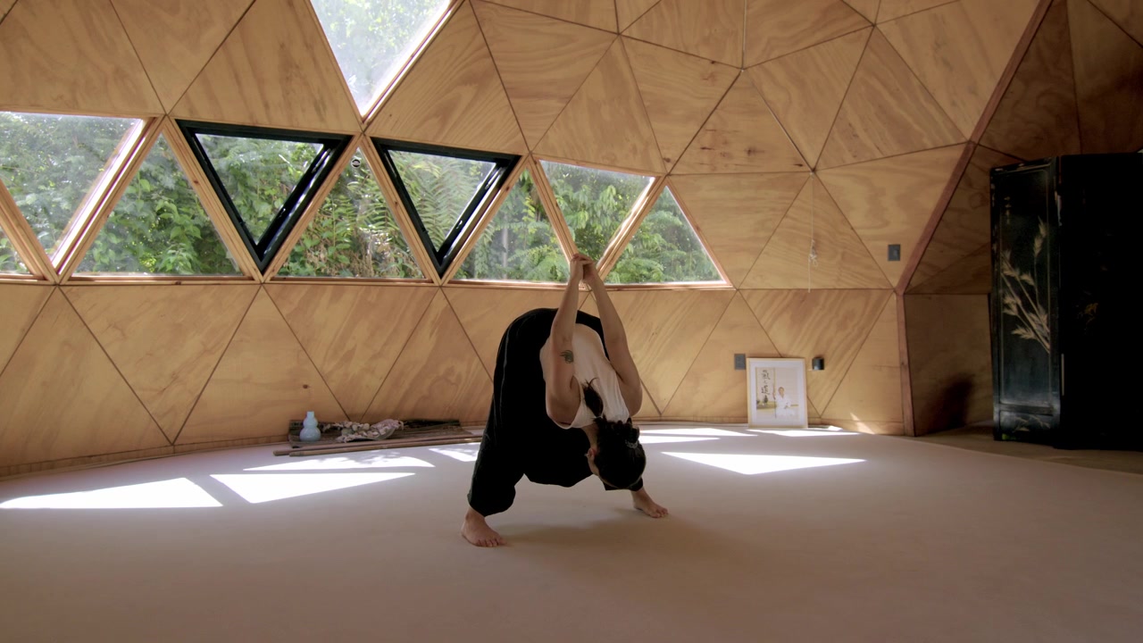 Una donna pratica yoga, allungandosi su e giù in uno studio esterno sereno e geometrico, concentrandosi sulla consapevolezza e sulla calma.