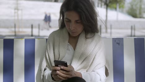 una mujer de mediana edad concentrada escribiendo un mensaje en su teléfono inteligente.