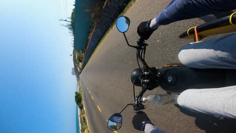 Vertical-De-Un-Joven-Explorando-El-Sudeste-Asiático-Con-Una-Tabla-De-Surf-En-Un-Moderno-Y-Rápido-Viaje-En-Moto-Por-Carretera