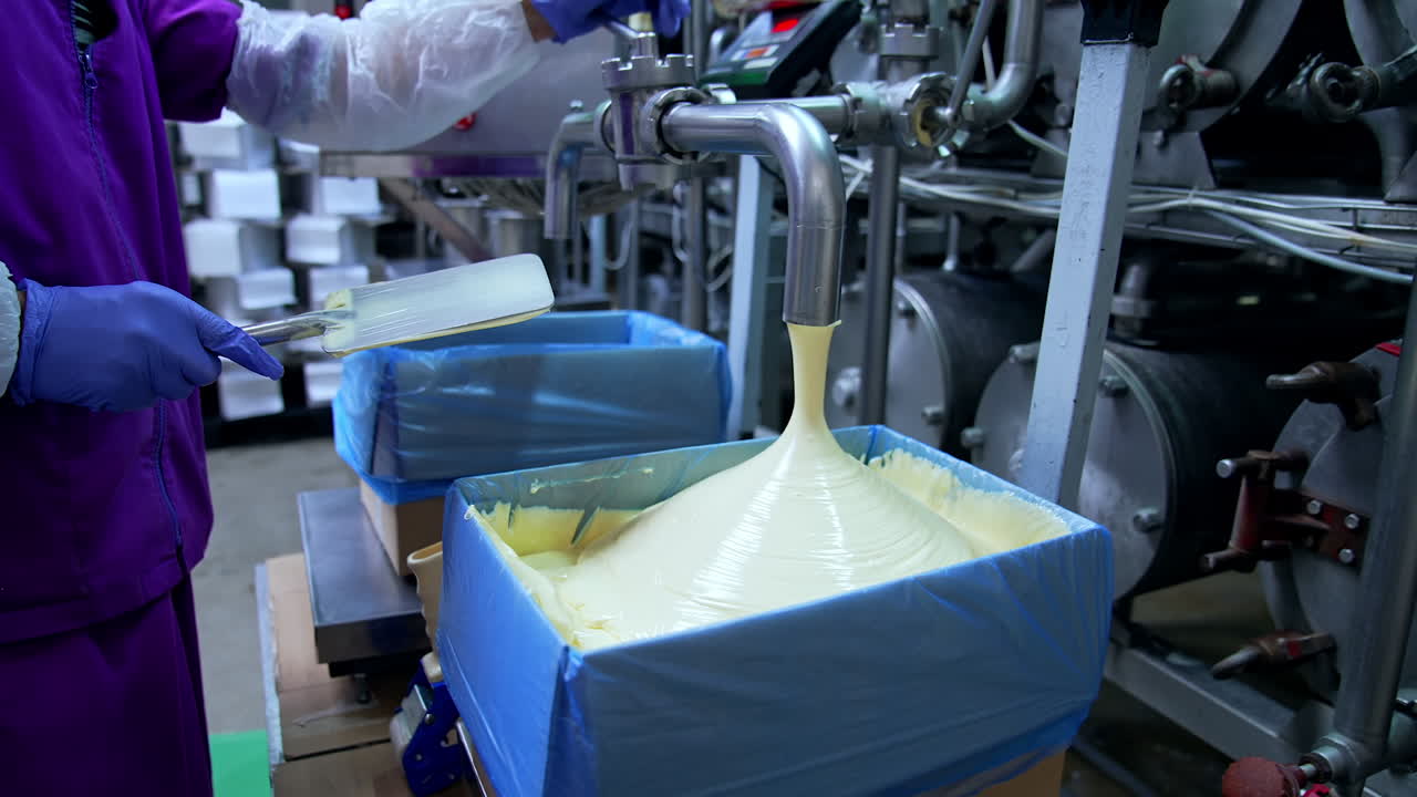 Making butter on a dairy factory. Industrial equipment at milk factory. Worker on a dairy production plant. Fresh smooth butter pouring from pipe into a box.