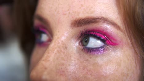 Unrecognizable-makeup-artist-work-in-beauty-studio.-Woman-applying-tone-using-brush.-Artist-make-a-makeup-for-redhead-model-with-freckles.-Close-up-of-eyes-of-a-pretty-girl-with-pink-glitering-make-up