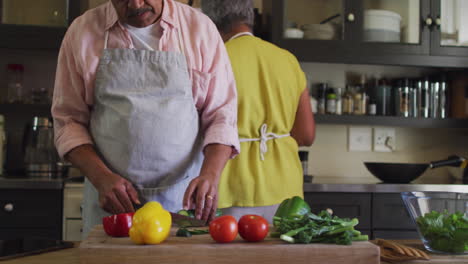 senior biracial couple wearing aprons preparing food in kitchen