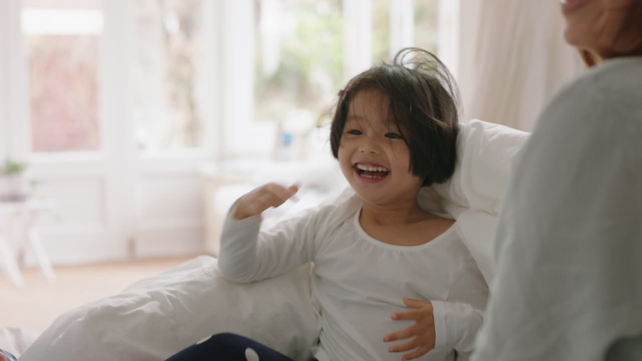 행복한 아시아 가족과 아이들이 침대에 뛰어들고 엄마와 아빠와 함께 놀고 주말 아침에 재미를 느끼고 흥분된 어린 아이들이 부모와 함께 집에서 게임을 즐기고 있습니다. 4k 영상