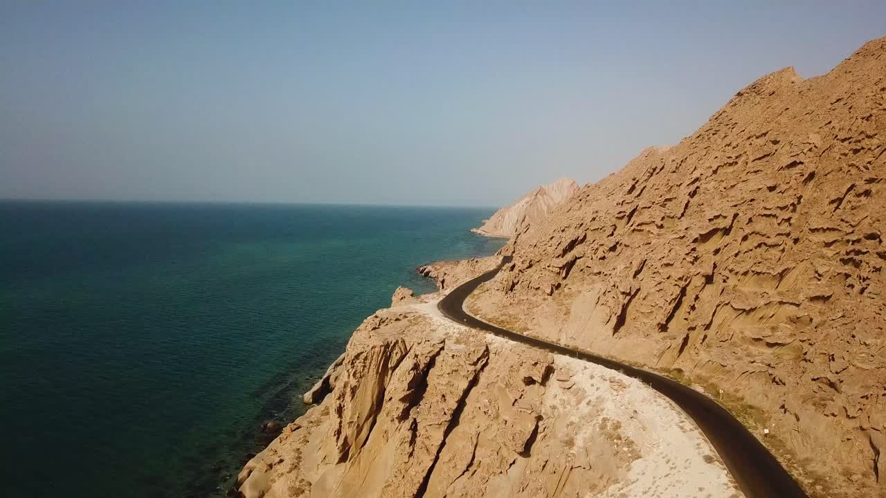 Splendida veduta aerea di un paesaggio costiero con scogliere rocciose erose, montagne e spiagge, lungo una strada panoramica nel Golfo Persico, Iran. Un orizzonte meraviglioso per un'avventura marina e un viaggio on the road all'insegna dell'ospitalità araba e della pace.