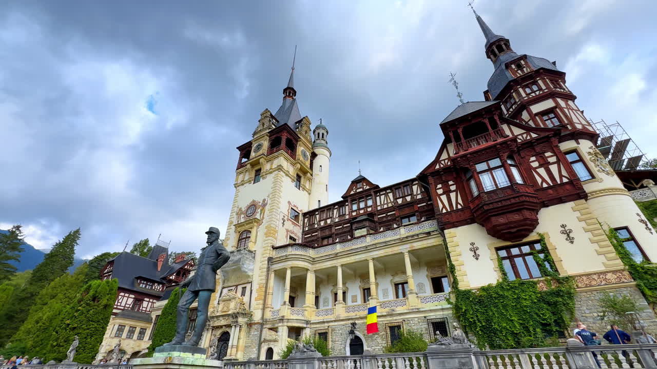 Sinaia, Romania, 17 July 2025: Front facade of Peles Castle in Romania. Wide view of the front facade of Peles Castle in Sinaia with Romanian flag and statue in front