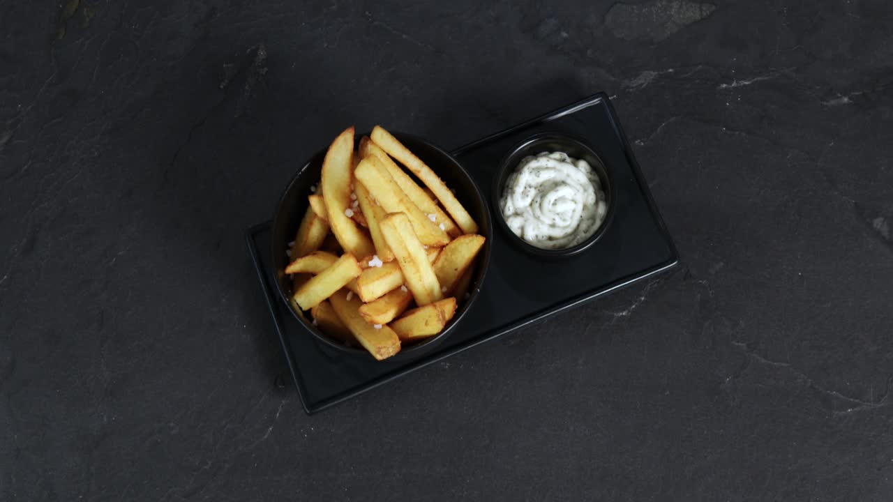 French fries with salt next to a mug of mayonnaise are presented on a rotating plate