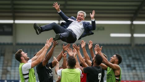 a celebratory moment captured: a thrilled coach is joyfully raised by his team after a successful game, showcasing team spirit and unity