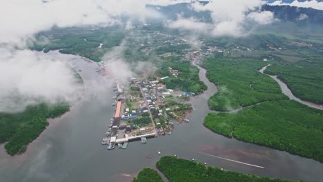 fishing village revealed through the clouds using an aerial drone over lang thung nang dam river and mangroves at khura buri district province, thailand