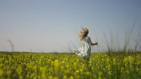 young blonde girl in white dress runs through tall grass and flower field happy