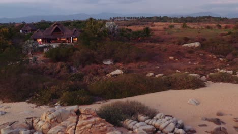 Drone-flies-over-crashing-waves-on-the-coast-of-Oaxaca-Mexico,-towards-and-above-luxury-villa-4K-aerial