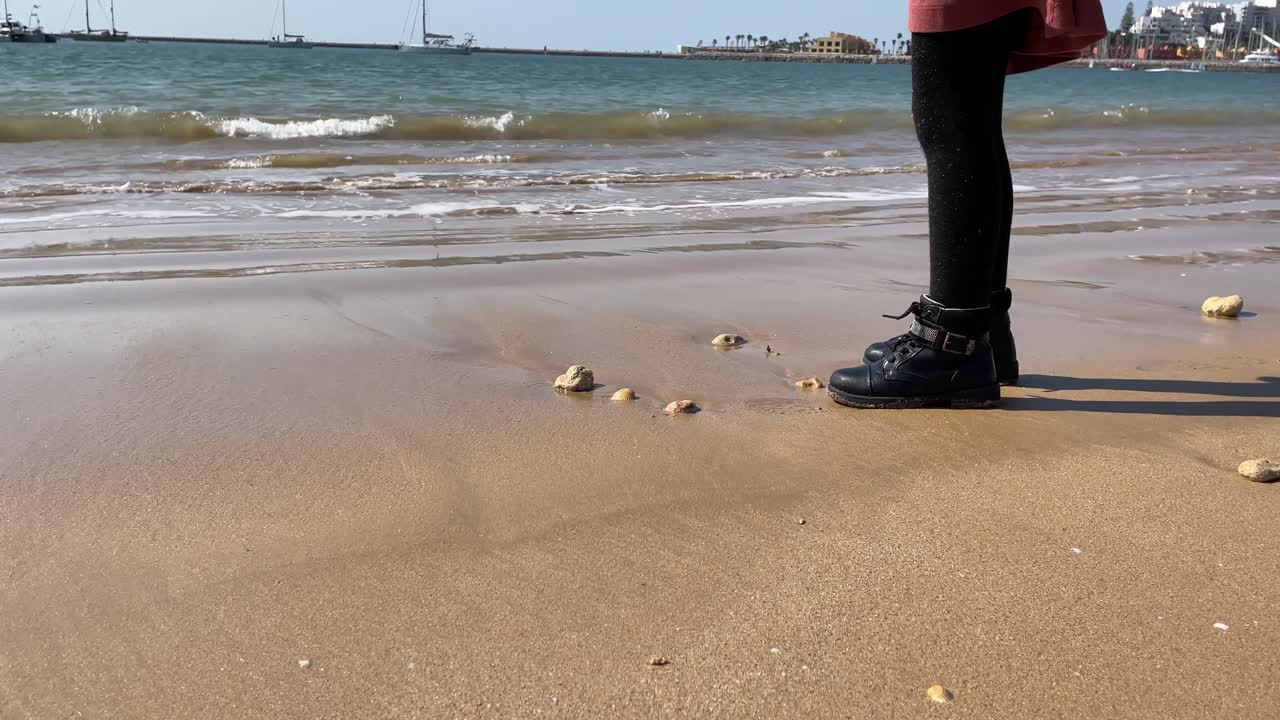 아침에 젖은 모래에서 무언가를 집는 아기 소녀가 보이는 해변의 정적인 장면