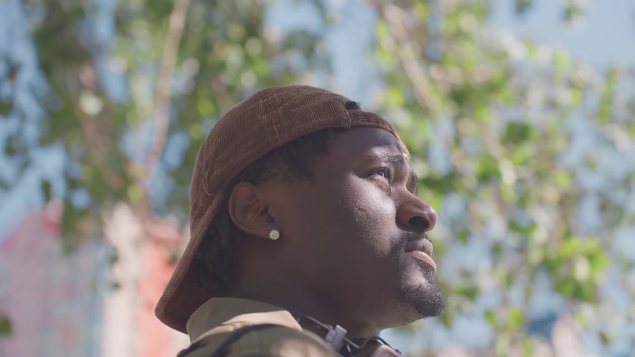 Close up of man wearing orange cap and earphones looking around outdoors with trees and sky in background. subject remains stationary showing consistent profile view with slight head