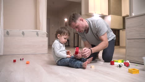 zoom in shot of a baby and father sitting on the floor in the living room while playing with toys