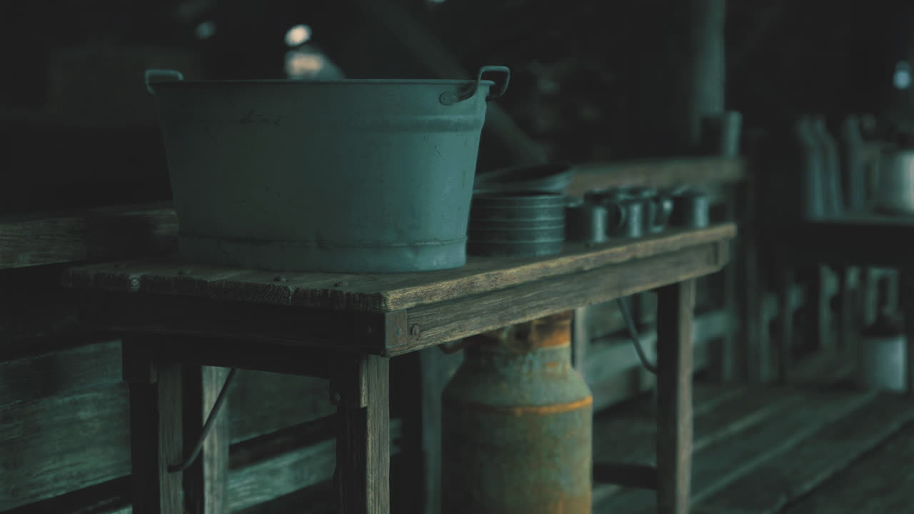 Dark wooden table with metal utensils and a bucket in a rustic setting