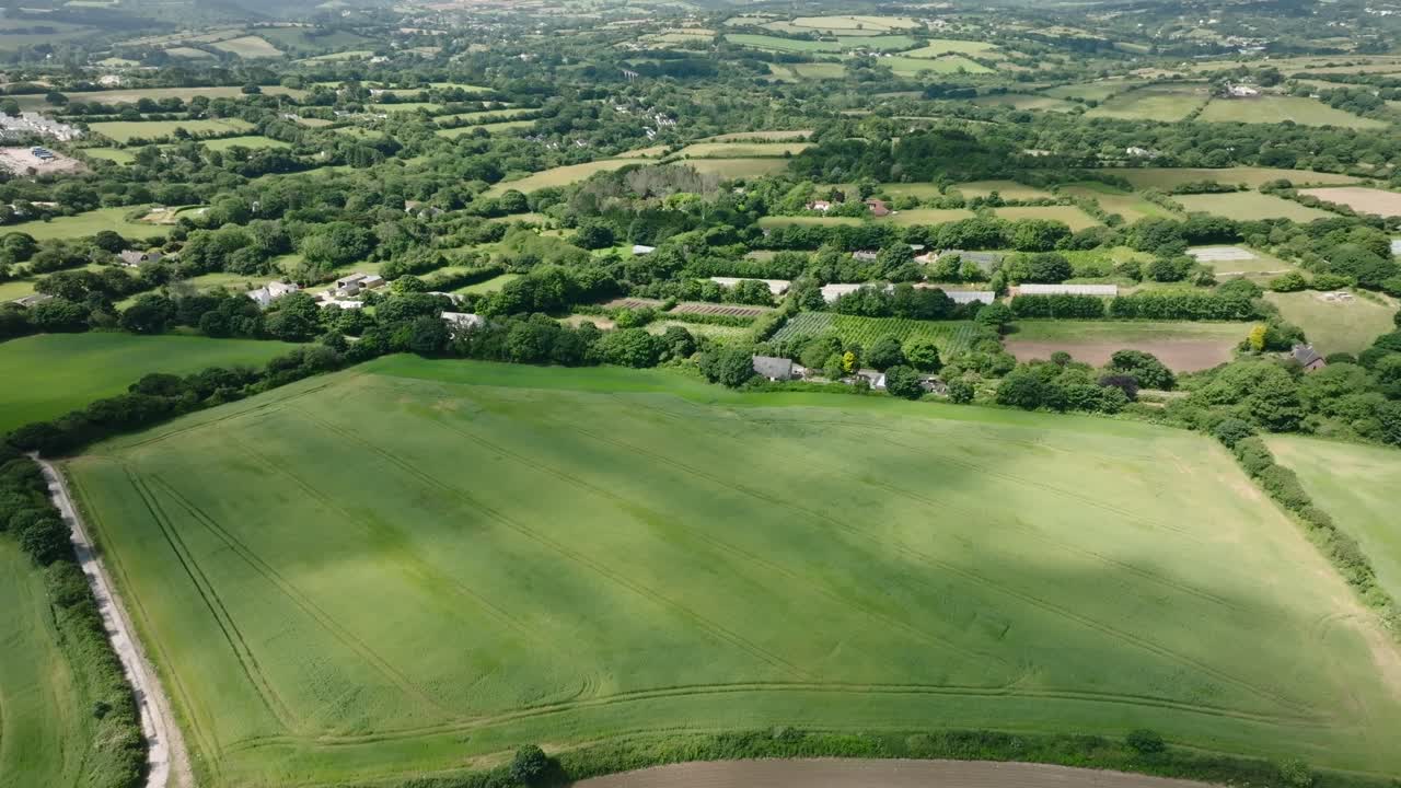 Cloud shadows moving over tended farmland fields surrounded by hedgerows with patchwork fields beyond. Summer, Cornwall, UK.