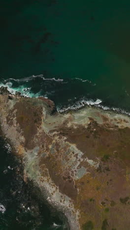 mountainous landscape crossed by roads with moving cars. sea-green water of pacific ocean washing the bare rocks. sunny day footage. vertical video