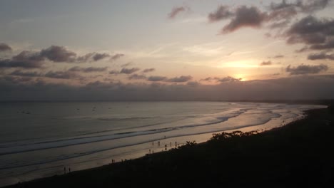 Aerial-view-of-sunset-beach-with-the-waves-lapping,-dramatic-sky-sunset-scenery