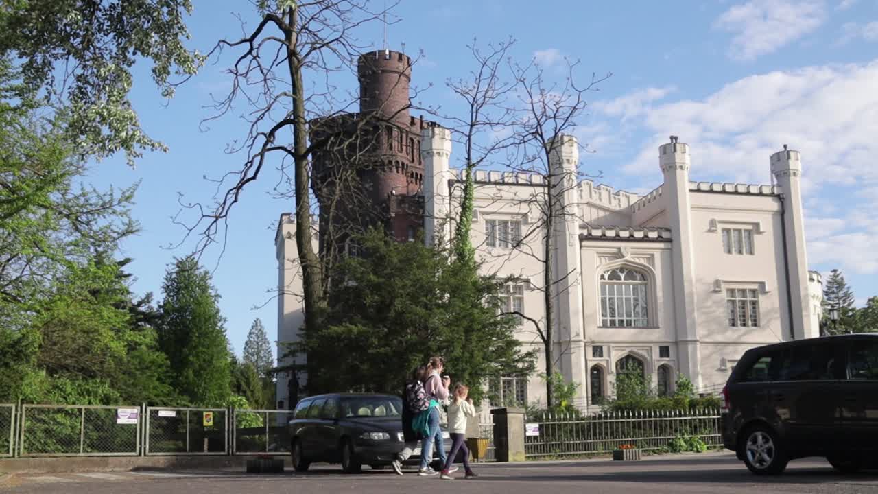 People walking in front of Kórnik castle in Western Poland on sunny spring day.