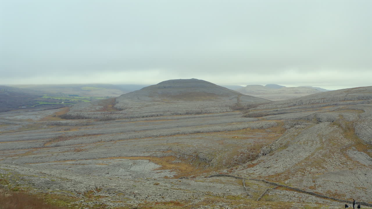Aerial dolly shot of limestone hills in Burren National Park, featuring hikers admiring the scenery
