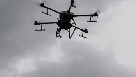 professional agriculture drone flying under dark cloudy sky, low angle, slow motion