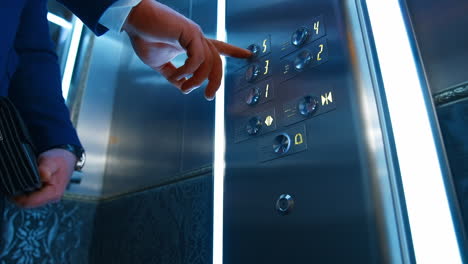 Man`s hand presses floor buttons in elevator. Unrecognizible man in suit pushes floor button. Selective focus.
