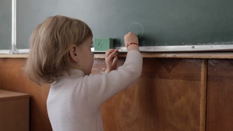 girl drawing at blackboard using a chalk in classroom. education process