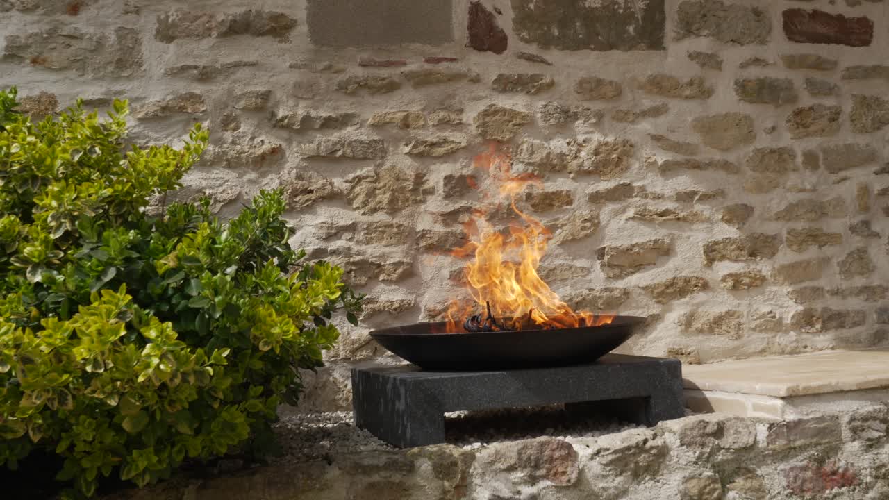 Fuoco che brucia vivacemente in una padella di metallo sollevata su una superficie nera davanti a un muro, tradizionale.