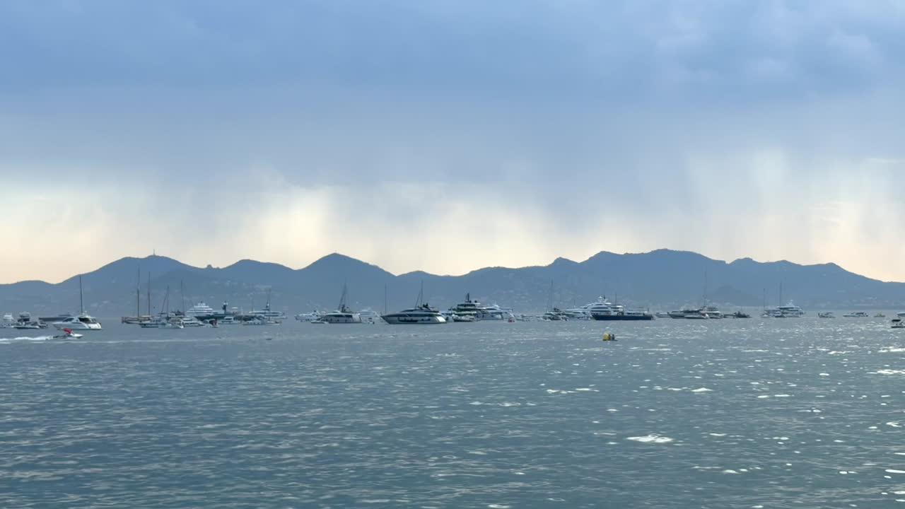 Yachts anchored off the coast of Cannes, mountains and rainy sky in background. Static