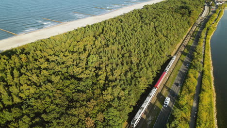 Aerial-Cinematic-view-on-train-between-green-forest-Baltic-Sea-and-guld-of-Gdansk,-Kuznica-Poland