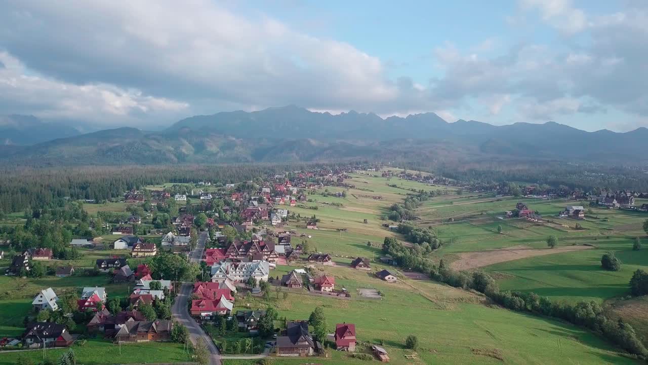 Aerial of small resort in Polish Tatra Mountains. Drone flies away from the buildings, slightly rotating, revealing the majestic mountain range.