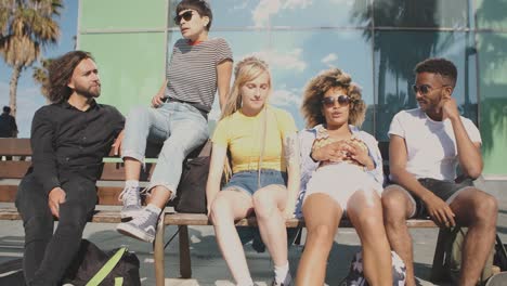 cheerful modern friends on bench in summertime