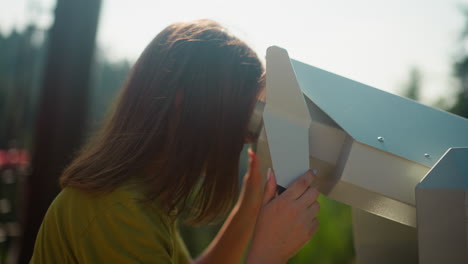 woman at observation deck looks through binoculars. lady enjoys leisure activities with amazing landscape of nature and dense woodland on sunny summer day