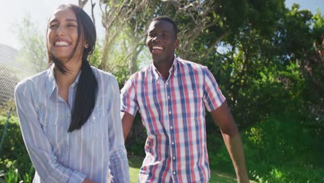 Video-of-happy-diverse-couple-holding-hands-and-walking-in-sunny-garden-smiling