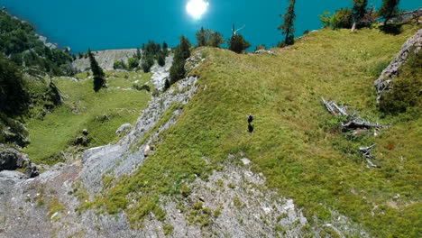 revealing aerial shot of a woman hiking on the edge of a mountain with a beautiful blue lake in the background