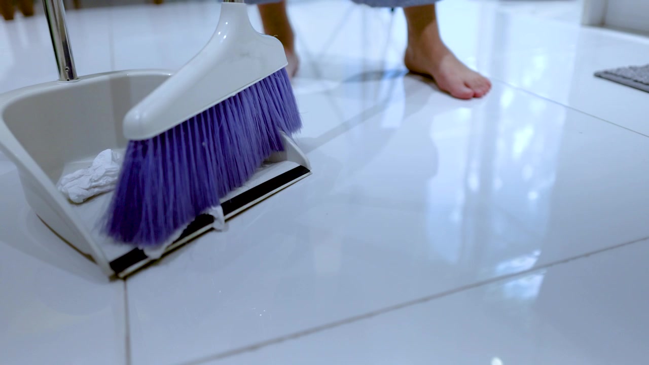 Low angle shot of bare feet standing while sweeping trash into a white dustpan