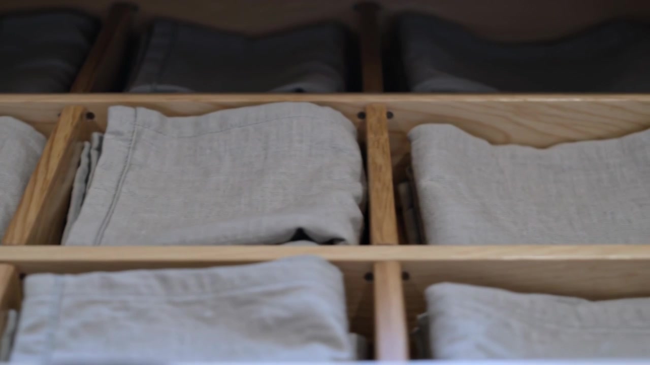 Panning camera revealing wooden grid drawer in home, to show organized gray linens