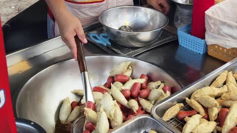 street food vendor preparing fried sausages and fish cakes